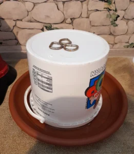 ein kleiner Popcorn-Eimer, ein großer Kunststoff-Blumenuntersetzer, 3 Stahlringe (oder dicke flache Knöpfe)